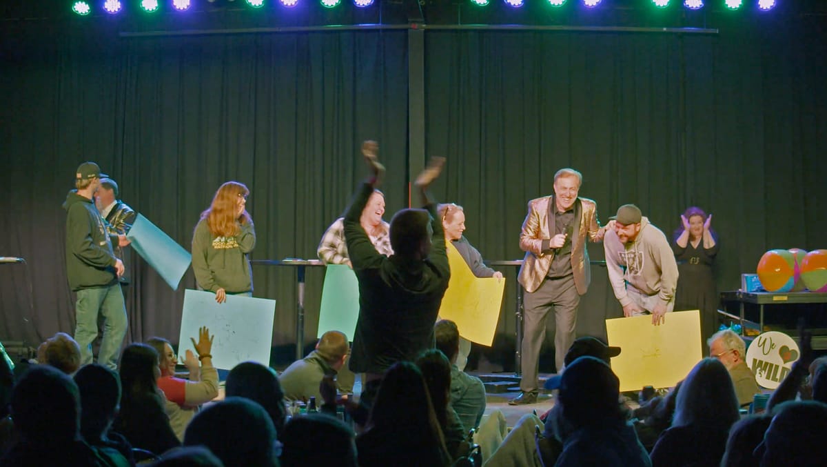 Brett Walkow and Dan Deibert on stage with laughing contestants holding up answer cards