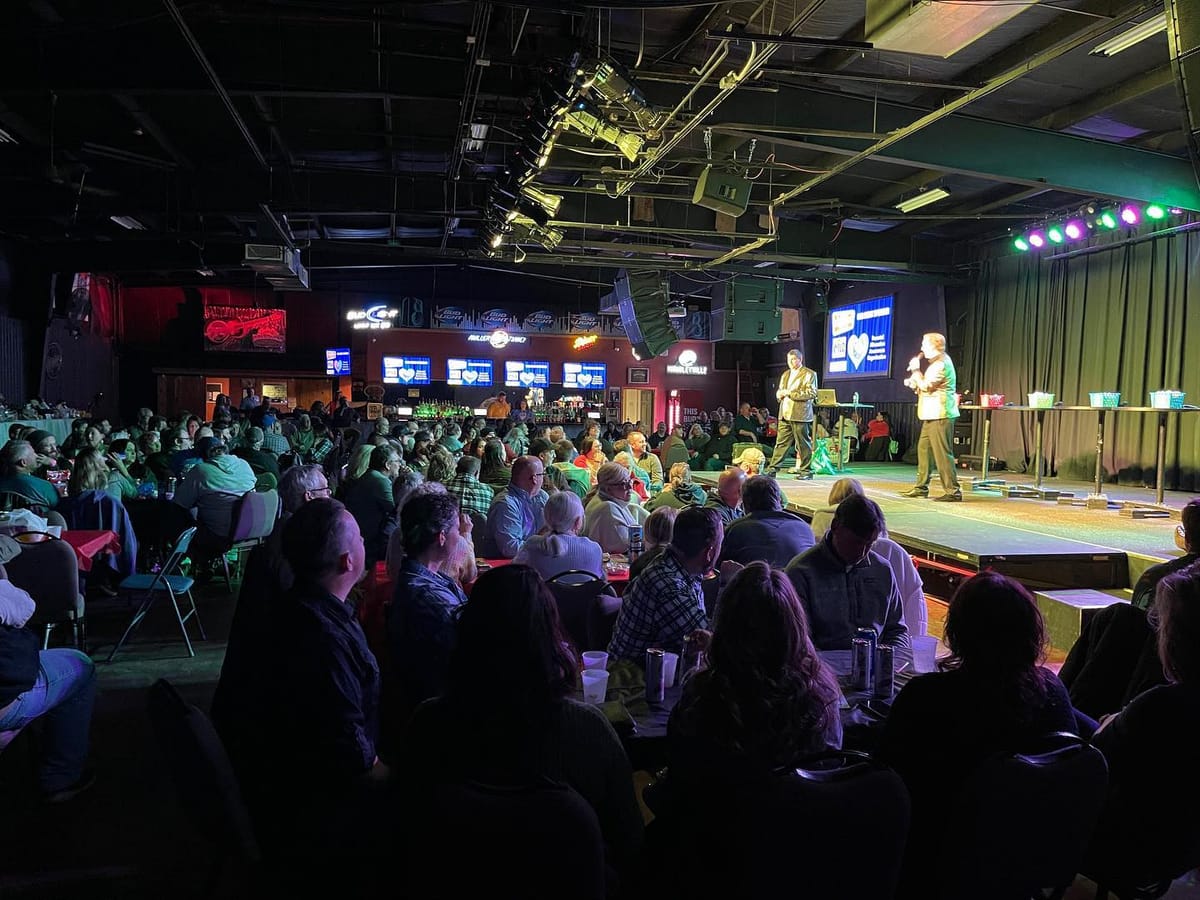 The hosts on a lit stage in front of a full room