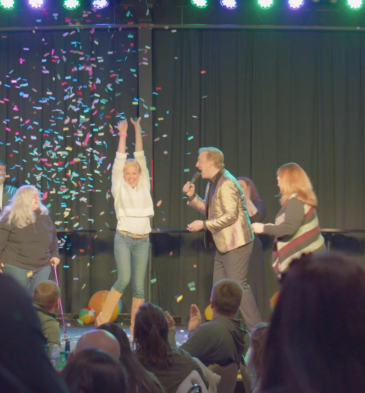 A contestant on stage with both arms in the air as confetti falls